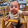 baby, child, high_chair, tongue_out, indoor, cafe, wooden_chair, person, cute, playful, infant, flooring, table, furniture, hand, face, clothing, seatbelt, expression, smile