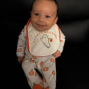 Logan joined the competition — help win amazing prizes! baby, child, smiling, halloween, pumpkin, bib, clothing, onesie, footed_pajamas, black_couch, face, person, happy, indoors, young_child, seated, cute, holiday, festive, costume