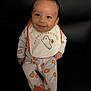 baby, child, smiling, halloween, pumpkin, bib, clothing, onesie, footed_pajamas, black_couch, face, person, happy, indoors, young_child, seated, cute, holiday, festive, costume
