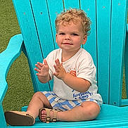 Matthew joined the competition — help win amazing prizes! toddler, child, curly_hair, smiling, clapping, sitting, chair, adirondack_chair, blue_chair, outdoor, grass, casual_clothing, tshirt, shorts, sandals, summer, happy, playful, cute, portrait