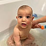 adult_hand, baby, bath_time, bath_toy, bathtub, blurred_background, child, cute, face, hand, infant, portrait, rubber_duck, sitting, skin, surprised_expression, tiles, water, wet, wide_eyes
