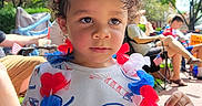 Demerious is registered to the contest to win money with this photo: child, patriotic, red_white_blue, headband, flower_lei, outdoor, sunny, curly_hair, tshirt, people, grass, chairs, event, celebration, daytime, sidewalk, trees, relaxed, casual, family