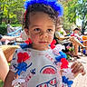 child, patriotic, red_white_blue, headband, flower_lei, outdoor, sunny, curly_hair, tshirt, people, grass, chairs, event, celebration, daytime, sidewalk, trees, relaxed, casual, family