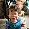 Demerious is registered to the contest to win money with this photo: toddler, child, smile, curly_hair, blue_shirt, dinosaur_print, indoor, carpet, chair, jacket, drawer, table, snack, happy, person, furniture, living_room, wood, clutter, portrait