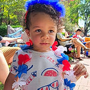 Demerious is registered to the contest to win money with this photo: toddler, child, outdoor, party, festive, headband, lei, red_white_blue, curly_hair, summer, celebration, people, sitting, grass, sidewalk, daylight, patriotic, balloons, clothing, portrait