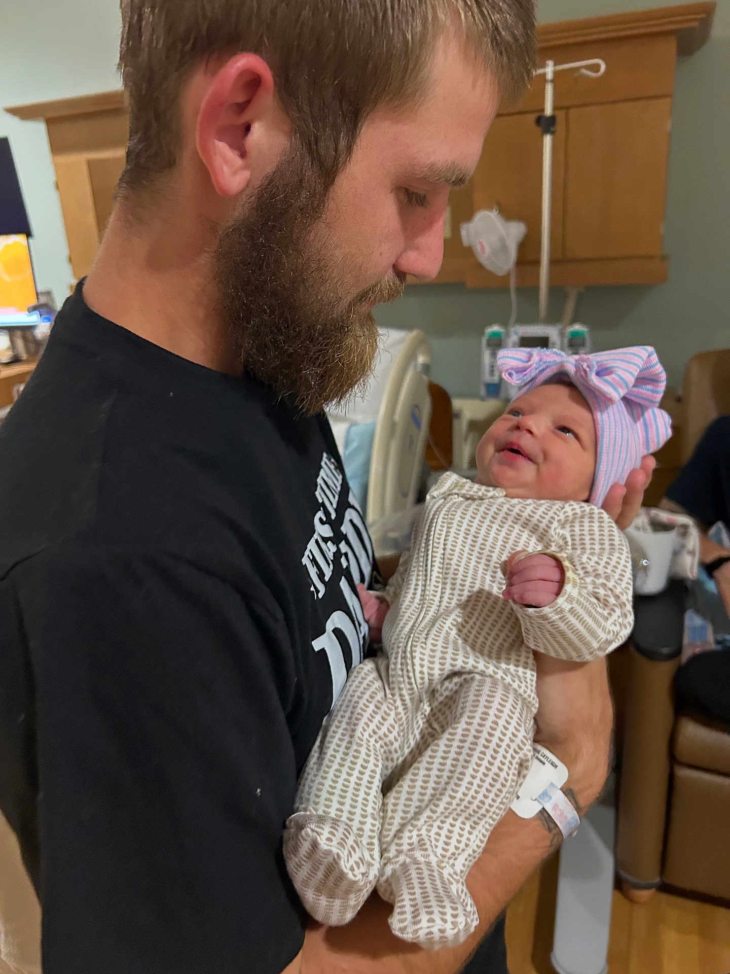 Blakelynn Elizabeth is registered to the contest to win money with this photo: man, baby, newborn, hospital, beard, smile, holding, bow_hat, medical_equipment, bed, black_shirt, infant, portrait, indoor, care, family, love, person, clothing, warmth