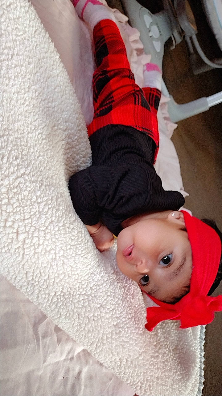 Delilah is registered to the contest to win money with this photo: baby, baby_toddler_clothing, carmine, child, comfort, flooring, foot, gesture, headwear, human_body, human_leg, knee, leg, linens, nail, pattern, person, sitting, sleeve, toddler