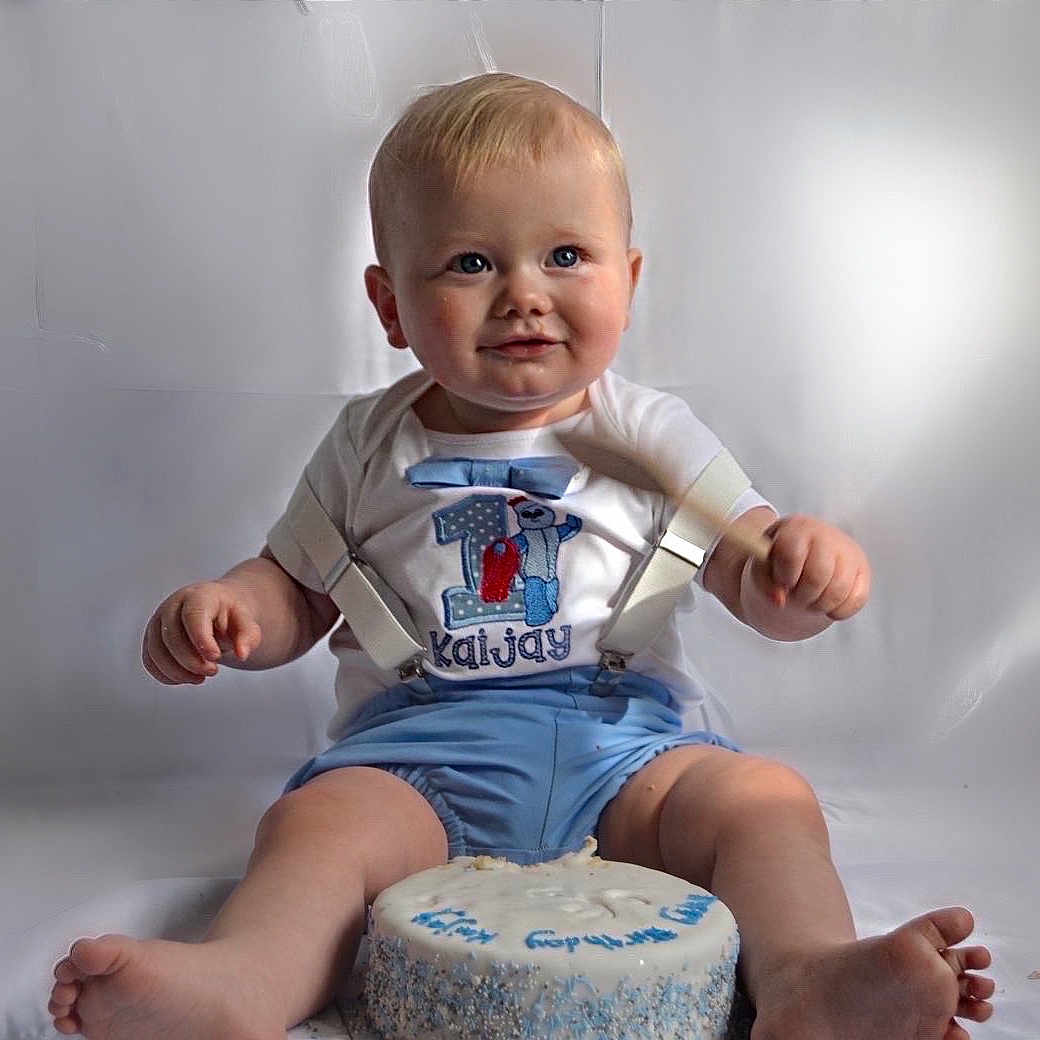 Kaijay joined the competition — help win amazing prizes! baby, birthday_cake, blue_shorts, cake, celebration, child, clothing, cute, face, feet, first_birthday, hands, happy, indoor, light_background, portrait, sitting, smiling, suspenders, toddler