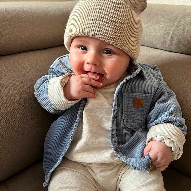 Sacha participe au concours pour gagner de l'argent avec cette photo : baby, beanie, bonnet, cap, clothing, coat, couch, face, furniture, happy, hat, head, jacket, jeans, pants, person, photography, portrait, sitting, smile