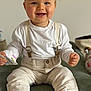 baby, child, smiling, blue_eyes, suspenders, pants, white_shirt, sitting, indoor, plush_toy, cozy, cute, happy, face, hands, footwear, home, portrait, infant, clothing