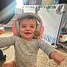 Sophie is registered to the contest to win money with this photo: baby, headphones, smile, carpet, playpen, toy, window, indoor, child, floor, person, happy, clothing, head, sitting, room, furniture, light, play, cute
