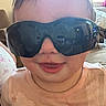baby, child, sunglasses, smile, face, indoors, pink_shirt, stain, couch, window, curtain, person, head, portrait, clothing, furniture, light, cheeky, cute, expression