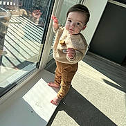 Gabriel is registered to the contest to win money with this photo: toddler, child, barefoot, indoor, sunlight, reflection, glass, window, door, carpet, sweater, pants, standing, curious, baby, person, young_child, casual_clothing, home, daylight