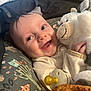 baby, smiling, stuffed_animal, pacifier, infant, cozy, cushion, patterned_fabric, close_up, happy, child, cute, soft_toy, indoors, portrait, baby_clothing, hand, face, newborn, comfort