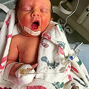 Uriah is registered to the contest to win money with this photo: newborn, baby, infant, hospital, blanket, medical_tube, yawning, face, hand, tape, footprint_pattern, wrapped, person, healthcare, bed, care, patient, closeup, skin, sleeping