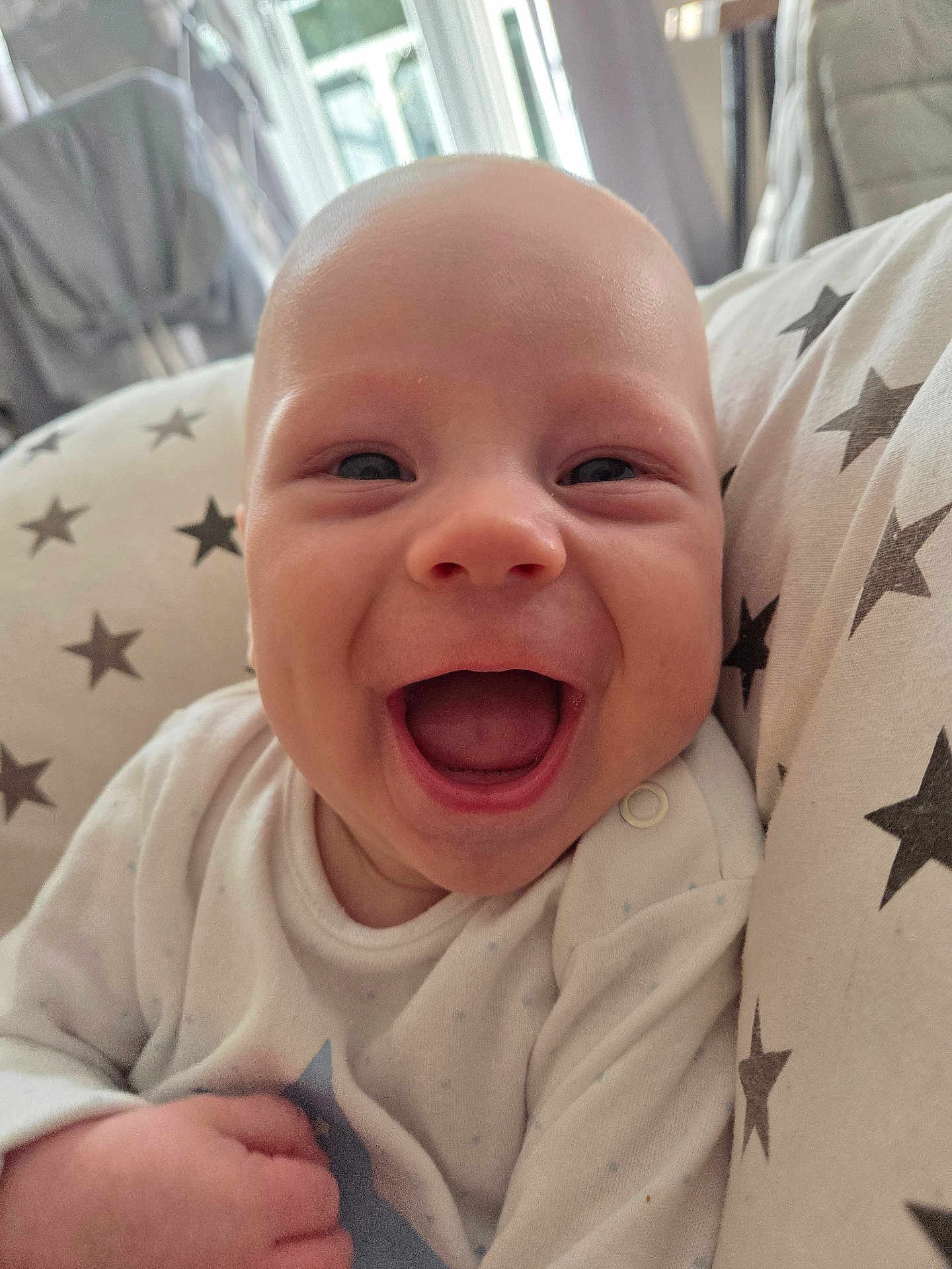 Freddie is registered to the contest to win money with this photo: baby, smiling, happy, infant, face, closeup, blanket, star_pattern, cozy, indoors, cute, child, newborn, person, expression, joy, soft_light, portrait, clothing, hand