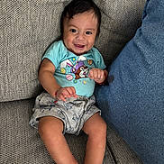 Anthony álvarez joined the competition — help win amazing prizes! baby, child, smiling, couch, blue_cushion, shorts, tshirt, cartoon_print, indoor, happy, infant, sitting, cute, skin, face, legs, hands, furniture, relaxed, comfortable
