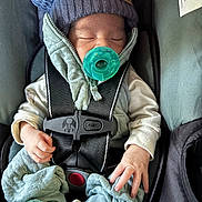 Anthony is registered to the contest to win money with this photo: baby, pacifier, car_seat, hat, knitted_hat, sleeping, infant, clothing, safety_harness, cute, hand, footwear, socks, indoor, child, bundle, cozy, resting, newborn, warm