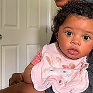 Elodie joined the competition — help win amazing prizes! arm, baby, big_eyes, child, closeup, clothing, curly_hair, cute, door, expression, face, giraffe_design, holding, indoor, infant, looking, person, pink_bib, portrait, skin