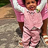 Trevon is registered to the contest to win money with this photo: baby, child, smiling, pink_clothing, vest, bow_tie, flower_corsage, white_shoes, adult_hands, supporting, outdoors, pavement, sunlight, happy, person, standing, cute, fashion, footwear, grass