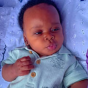 Lillian joined the competition — help win amazing prizes! baby, infant, face, hand, clothing, shirt, button, embroidery, blanket, blue_ribbon, lying_down, curly_hair, cute, expression, skin, portrait, child, indoors, soft_light, closeup