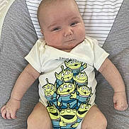 George is registered to the contest to win money with this photo: baby, infant, onesie, cartoon, alien, cushion, baby_seat, smile, face, arm, leg, skin, clothing, pattern, indoor, portrait, cute, child, person, relaxing