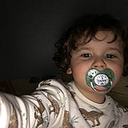 Ayden participe au concours pour gagner de l'argent avec cette photo : toddler, child, face, curly_hair, pajamas, dinosaur_pattern, pacifier, selfie, indoor, low_light, person, young_child, cute, baby, sleepwear, hand, portrait, expression, closeup, childhood