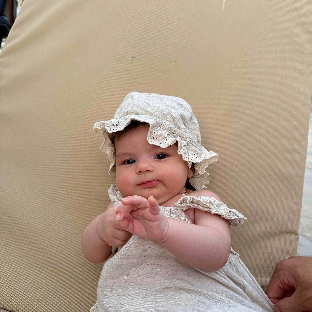 Lilia a rejoint le concours — aidez-le/la à gagner de superbes lots ! baby, beige, child, chubby_cheeks, clothing, curious, cushion, cute, dress, face, hand, hat, infant, outdoor, person, portrait, relaxed, sitting, skin, summer