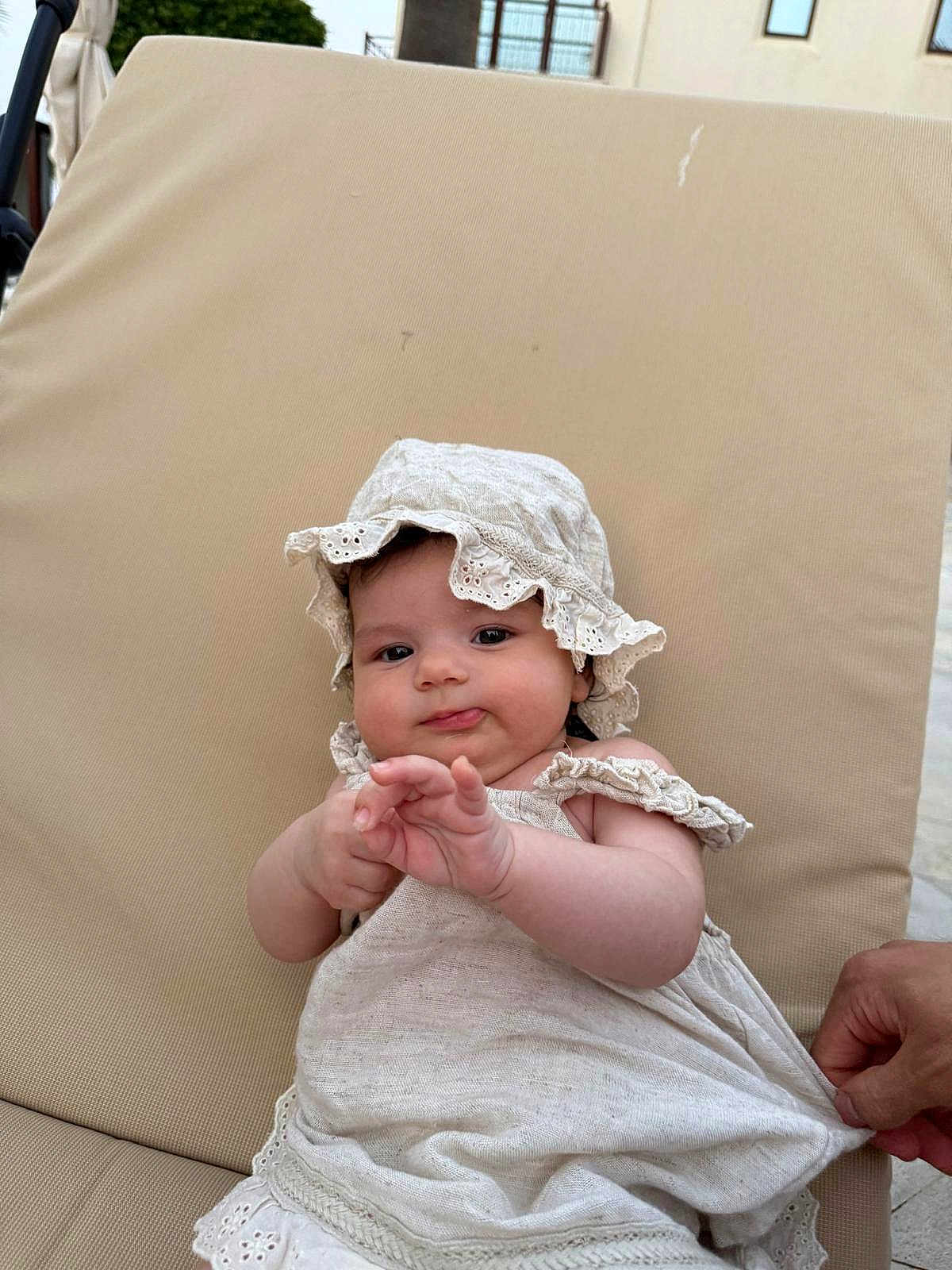 Lilia a rejoint le concours — aidez-le/la à gagner de superbes lots ! baby, infant, child, hat, dress, beige, cushion, hand, skin, face, outdoor, person, cute, summer, clothing, portrait, sitting, chubby_cheeks, curious, relaxed