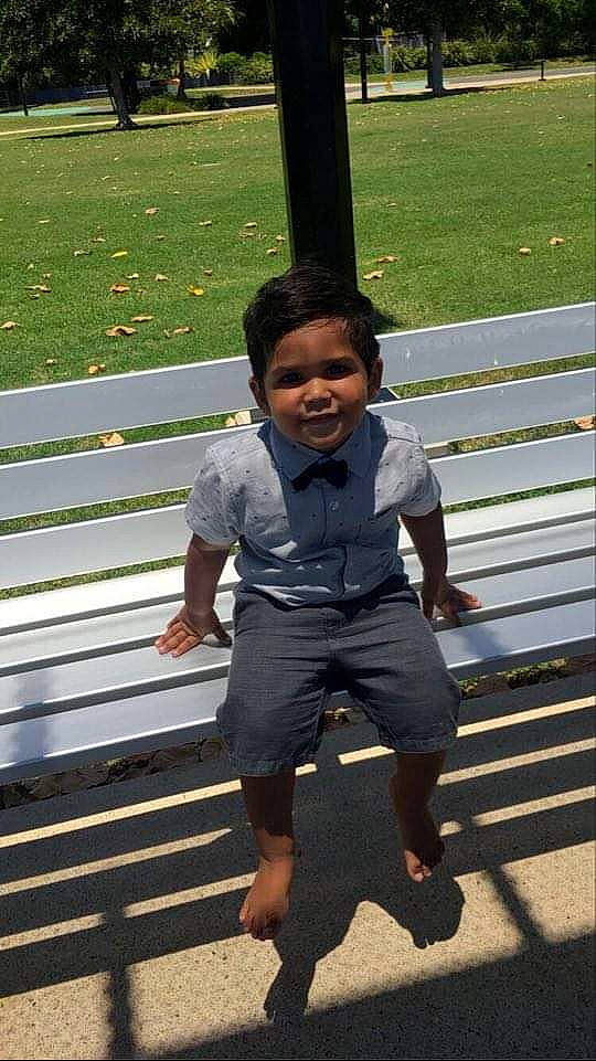 Jedediah is registered to the contest to win money with this photo: bench, child, foot, fun, grass, happy, human_leg, leisure, outdoor_bench, pedestrian, people_in_nature, person, plant, recreation, sitting, smile, standing, thigh, toddler, tree