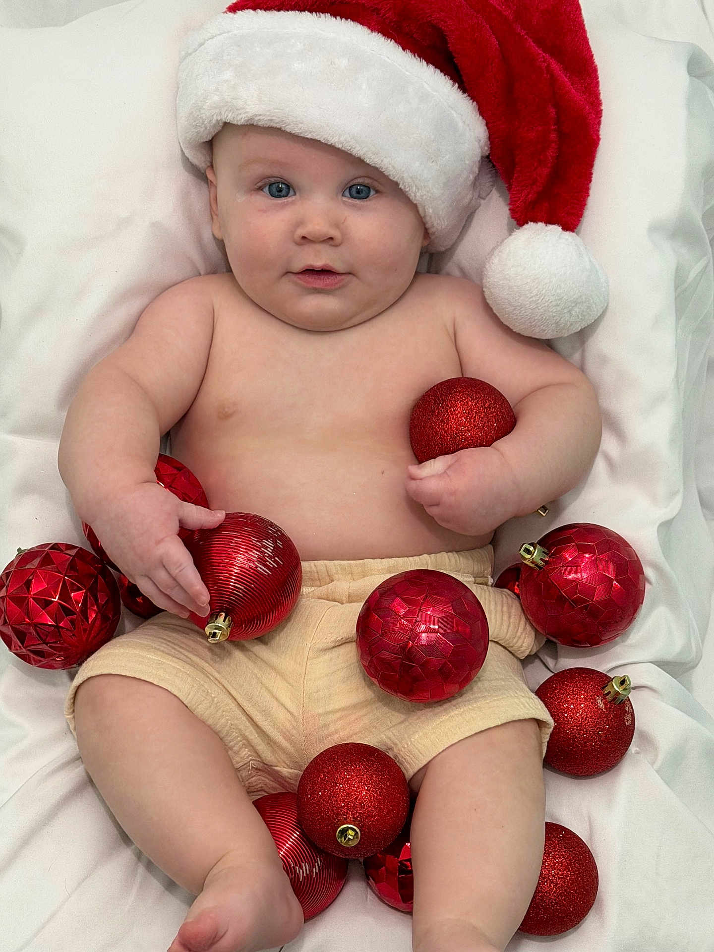 Joseph joined the competition — help win amazing prizes! baby, santa_hat, christmas_ornaments, red_balls, blanket, holiday, festive, cute, infant, smiling, blue_eyes, chubby, skin, shorts, holiday_decor, celebration, indoors, portrait, child, holiday_hat