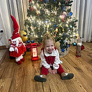 Tamari participe au concours pour gagner de l'argent avec cette photo : child, toddler, christmas_tree, holiday_decorations, gnome, lantern, wooden_floor, smiling, sitting, indoors, festive, lights, ornaments, red_clothing, white_clothing, curtains, home, celebration, happy, toy_car