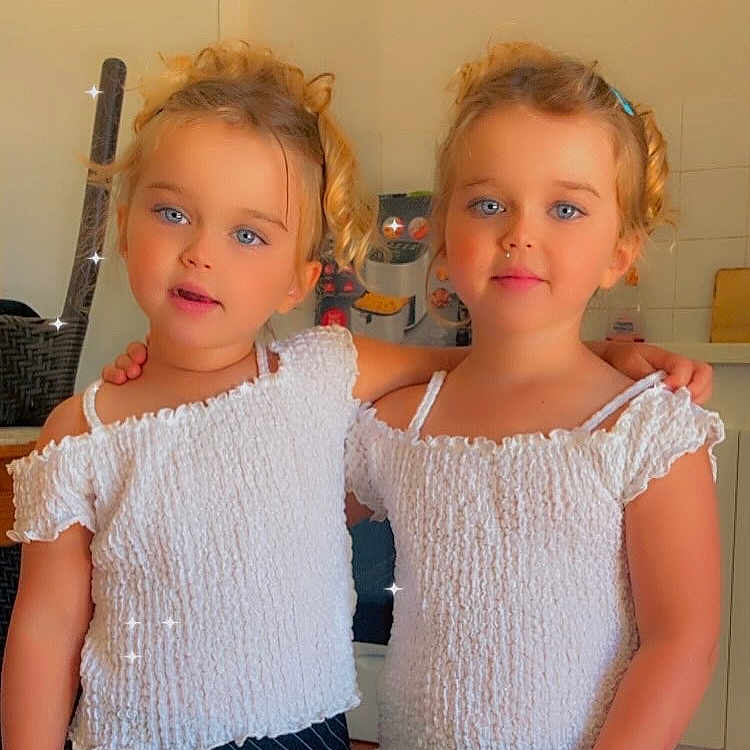 Lina Luna a rejoint le concours — aidez-le/la à gagner de superbes lots ! arm_in_arm, blonde_hair, blue_eyes, casual, child, curly_hair, cute, face, fashion, girl, happy, indoor, kitchen, person, portrait, smiling, sparkles, toddler, twin, white_top