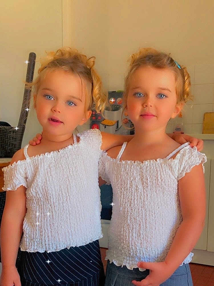 Lina Luna a rejoint le concours — aidez-le/la à gagner de superbes lots ! arm_in_arm, blonde_hair, blue_eyes, casual, child, curly_hair, cute, face, fashion, girl, happy, indoor, kitchen, person, portrait, smiling, sparkles, toddler, twin, white_top