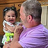 Nala Ann is registered to the contest to win money with this photo: baby, child, man, holding, smiling, hair_clips, purple_shirt, kitchen, wooden_cabinet, happy, indoor, portrait, family, cute, affection, person, love, tenderness, casual, people