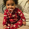 toddler, child, pacifier, pajamas, curly_hair, bed, blanket, pillow, indoor, smiling, cute, baby, sitting, red_clothing, animal_print, cozy, young_child, person, infant, happy
