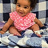 baby, child, infant, smiling, pink_clothing, polka_dot, curly_hair, blanket, checkered_pattern, blue_and_white, sitting, cute, happy, indoors, portrait, young_child, cozy, soft_texture, face, person