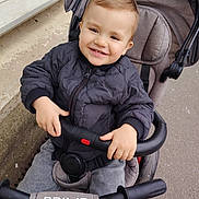 Maloë participe au concours pour gagner de l'argent avec cette photo : baby_stroller, baby_toy, casual_clothing, child, cute, daylight, happy, jacket, outdoor, person, portrait, seatbelt, sidewalk, smiling, stroller, toddler, transportation, urban, walking_path, young_child