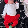 baby, blanket, child, clothing, cozy, cute, face, footwear, head, home, indoor, infant, lying_down, patterned_blanket, portrait, red_headband, red_leggings, red_skirt, sock, soft_toys