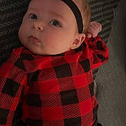 Nova joined the competition — help win amazing prizes! baby, infant, headband, flower, red_clothing, black_clothing, plaid_pattern, lying_down, curious_expression, chubby_cheeks, face, person, child, indoors, blanket, soft_texture, cute, young, portrait, casual_wear