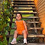 Dakohta is registered to the contest to win money with this photo: child, toddler, stairs, orange_clothing, sneakers, outdoor, greenery, brick_wall, smiling, happy, sitting, sunlight, metal_stairs, plants, casual, nature, portrait, person, daylight, cute