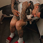 Duece is registered to the contest to win money with this photo: affection, black_and_white_dog, chair, corner, dog, domestic_animal, flooring, hugging, human, indoor, man, pet, red_slides, seated, shorts, tattooed_arms, tattooed_legs, tattoos, white_socks, white_tshirt