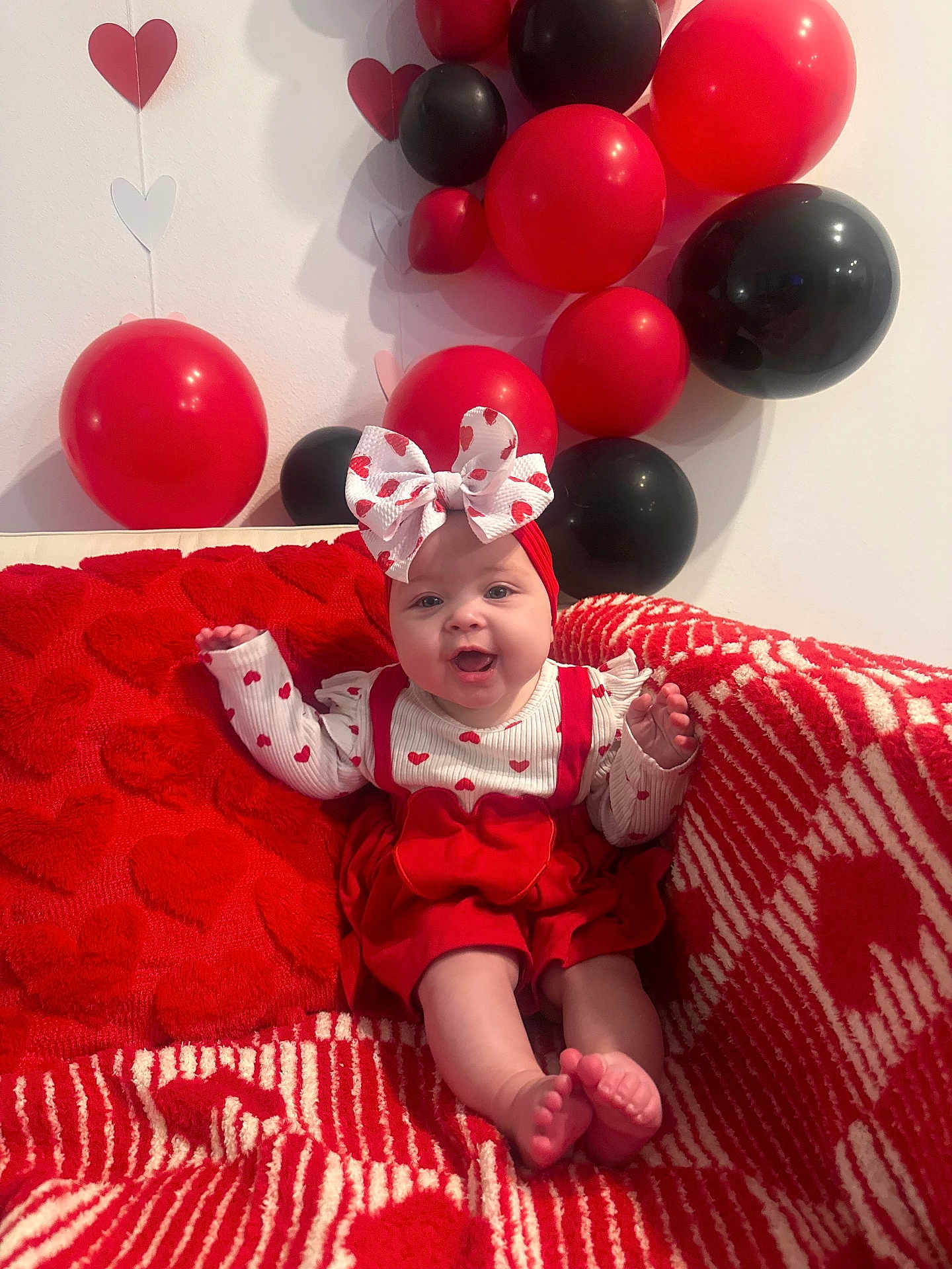 Alaiyah is registered to the contest to win money with this photo: baby, infant, child, bow, headband, red_dress, hearts_pattern, red_balloon, black_balloon, balloons, blanket, couch, smile, feet, sitting, valentines_decor, indoor, party_decor, cute, fabric_texture
