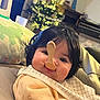 Himéa a rejoint le concours — aidez-le/la à gagner de superbes lots ! baby, child, face, spoon, wooden_spoon, curly_hair, bib, yellow_clothing, couch, pillows, living_room, christmas_tree, lights, holiday, indoor, cute, funny, smile, playful, portrait