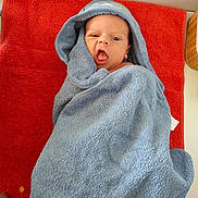 Ethan a rejoint le concours — aidez-le/la à gagner de superbes lots ! baby, child, towel, blue_towel, red_towel, hood, face, expression, mouth_open, eyes, skin, person, infant, lying_down, indoor, soft_texture, cute, cozy, wrapped, hand