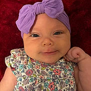 Leilani Cypress joined the competition — help win amazing prizes! baby, infant, headband, purple_bow, floral_dress, smiling, lying_down, red_blanket, cute, portrait, child, face, skin, hand, eyes, apparel, fashion, adorable, closeup, young