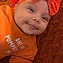 baby, infant, orange_clothing, headband, smiling, tongue_out, face, closeup, autumn_leaves, blanket, textile, cozy, cute, fall_theme, child, portrait, indoors, soft_texture, happy, person