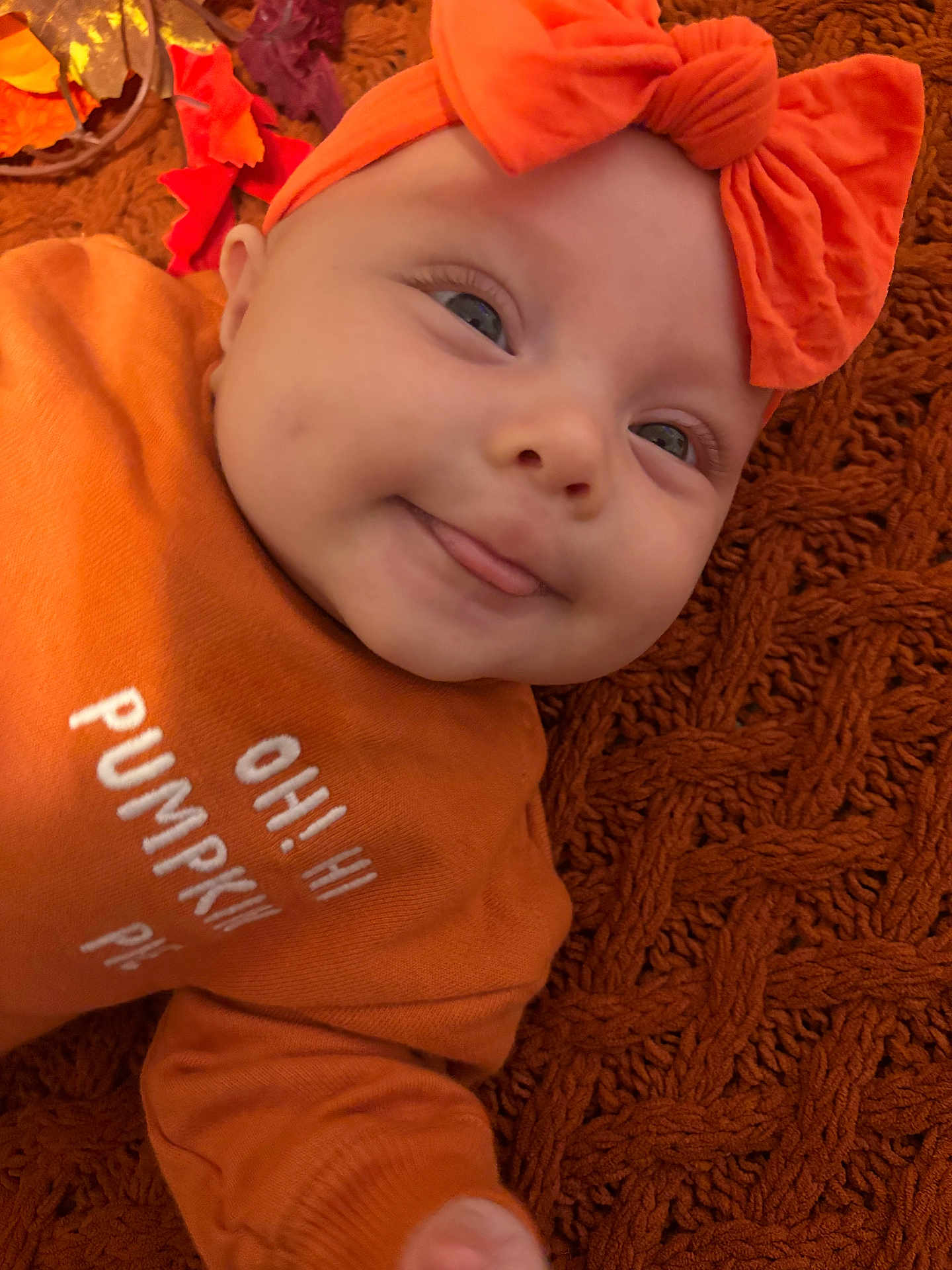 Leilani Cypress joined the competition — help win amazing prizes! baby, infant, orange_clothing, headband, smiling, tongue_out, face, closeup, autumn_leaves, blanket, textile, cozy, cute, fall_theme, child, portrait, indoors, soft_texture, happy, person