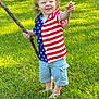 Jackson joined the competition — help win amazing prizes! toddler, child, grass, outdoor, stick, american_flag_shirt, shorts, barefoot, happy, smiling, curly_hair, summer, daylight, nature, play, person, greenery, lawn, casual_clothing, fun