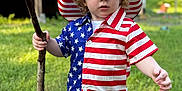 Jackson joined the competition — help win amazing prizes! child, toddler, boy, grass, outdoor, stick, hat, american_flag, shirt, shorts, summer, portrait, curly_hair, blue_eyes, casual_clothing, nature, daylight, person, standing, expression
